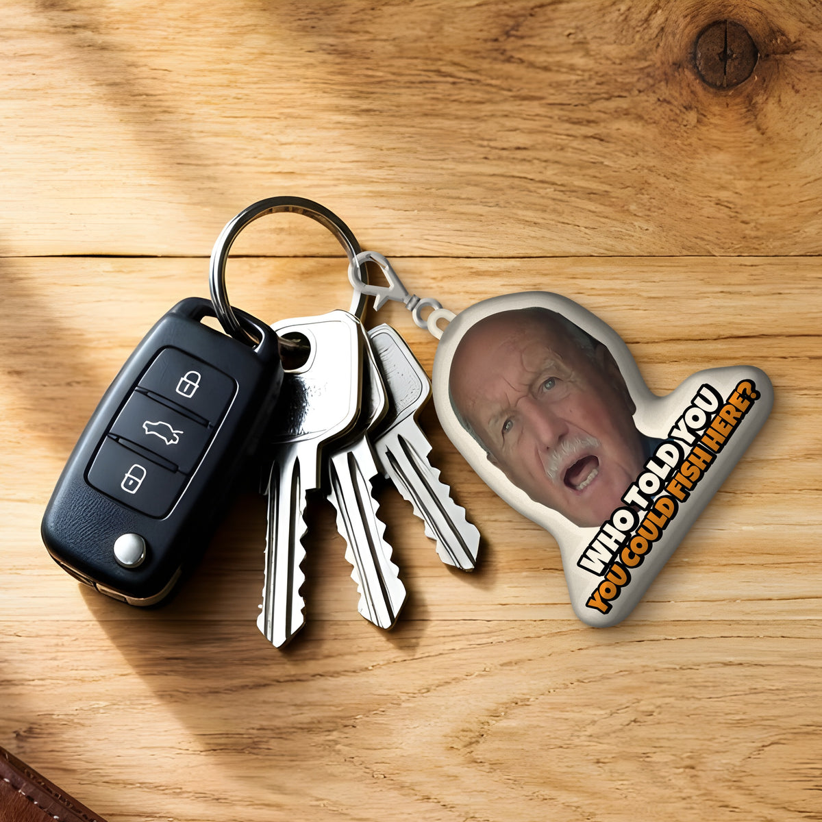 Who Told You You Could Fish Here? plush keychain clipped to car keys on a wooden desk
